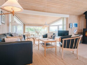 A cozy living room with a fireplace, wooden furniture, and large windows.