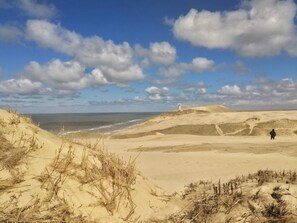 Un paysage côtier avec des dunes, un phare et une personne debout sur le sable.