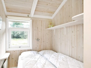 Une chambre avec un plafond en bois, une fenêtre donnant sur un paysage verdoyant, un lit avec une literie blanche et une étagère blanche au-dessus.