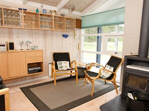 A cozy room with a wooden cabinet, two wicker chairs, a black and white patterned rug, and a wood-burning stove. - 10 Person Holiday Home in Albaek (Aalbaek)