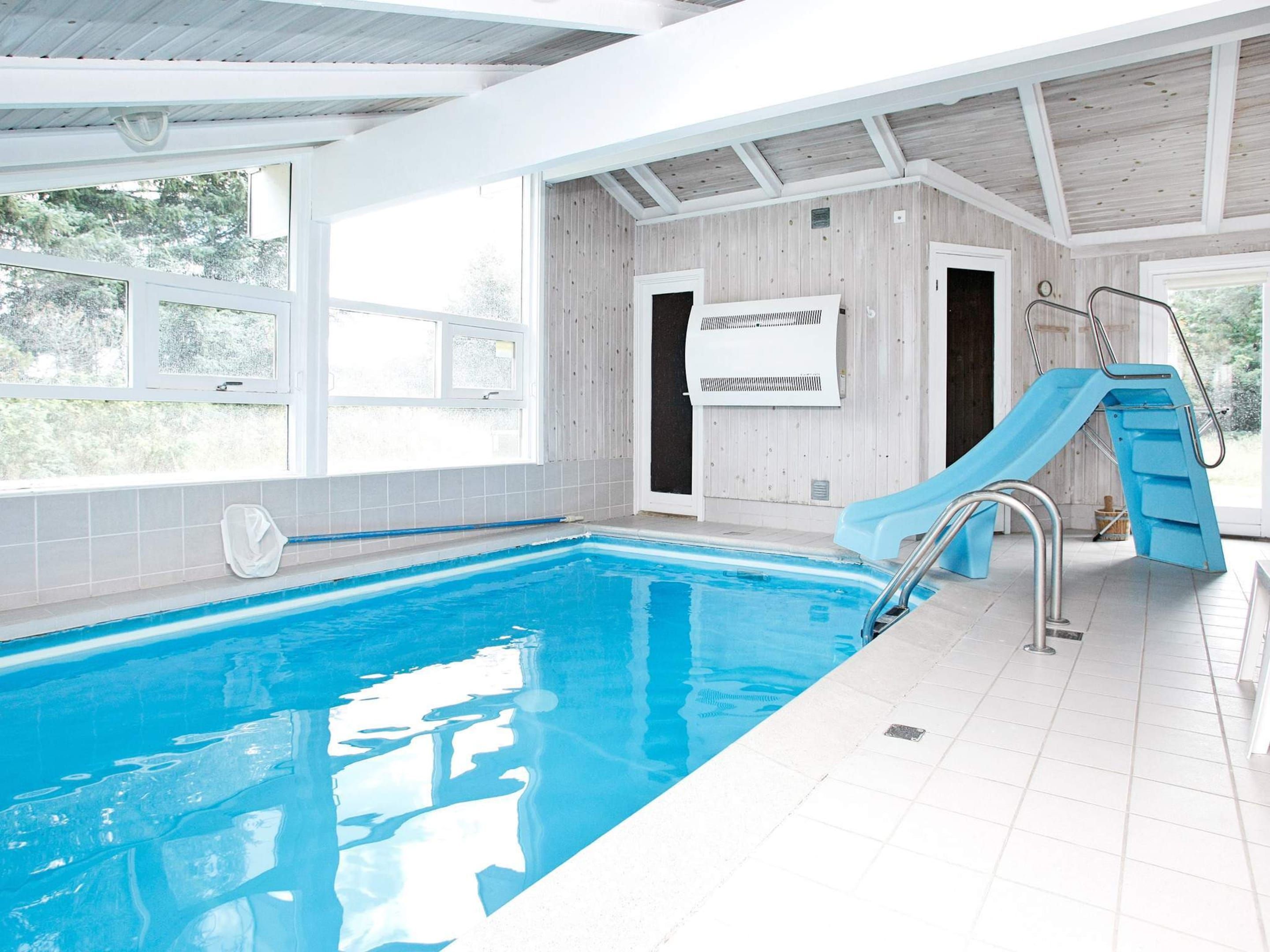 Une piscine intérieure avec un toboggan, un ventilateur de plafond et une vue sur l’extérieur.