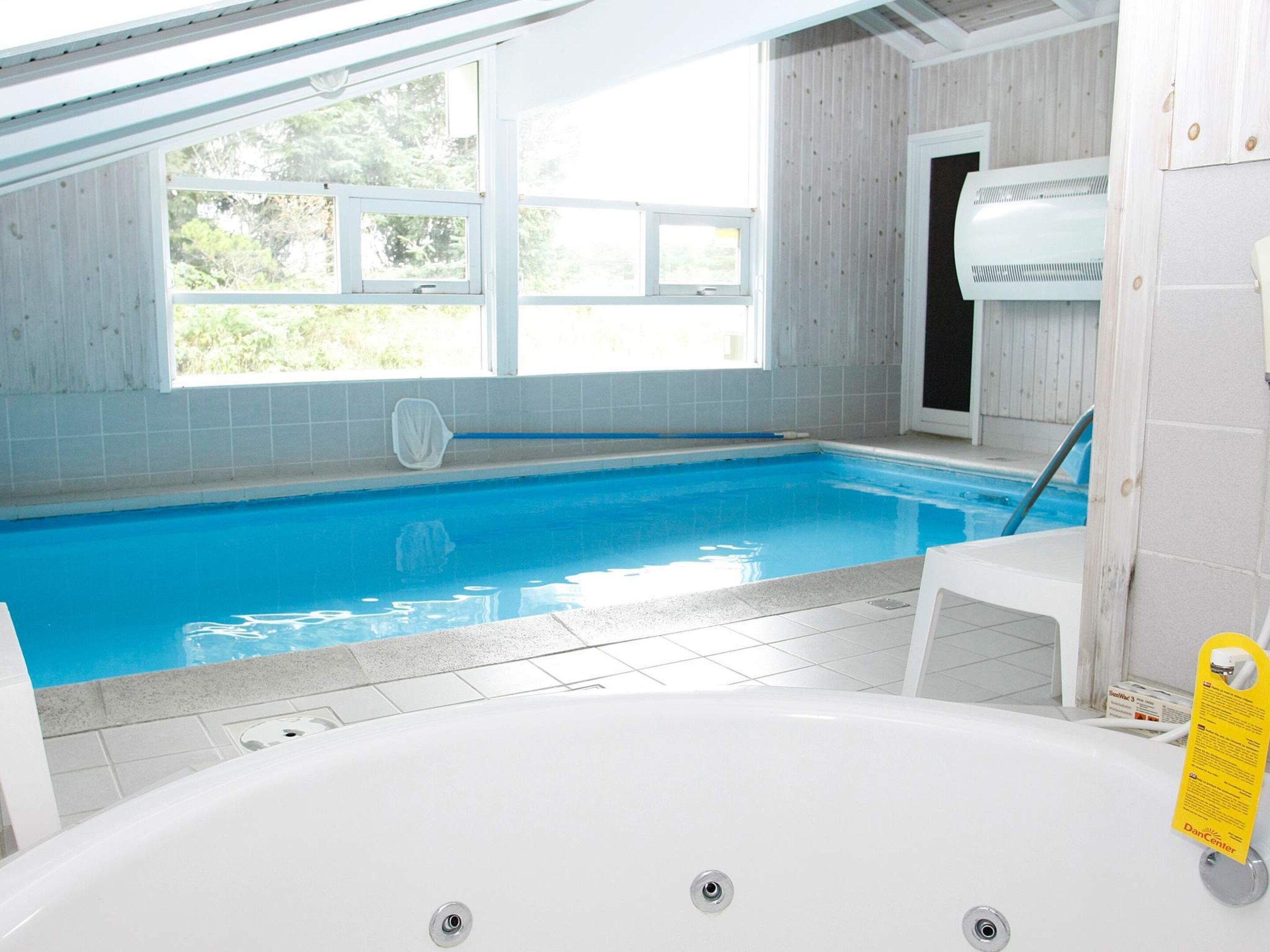 Une piscine intérieure offrant une vue dégagée sur l’extérieur, un jacuzzi blanc et une porte donnant accès à un sauna.