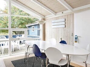A dining area with a large table and chairs, a wooden ceiling, and a view of a blue house through large windows. - 10 Person Holiday Home in Albaek (Aalbaek)