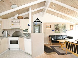 A modern kitchen with white appliances, wooden beams, and a black leather sofa in a living area. - 10 Person Holiday Home in Albaek (Aalbaek)