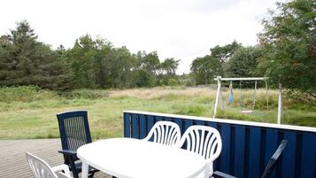 An outdoor seating area with a table and chairs, a swing set, and a wooden deck.