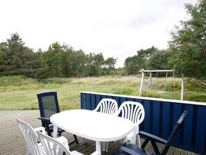 Et udendørs opholdsområde med borde og stole, et gyngestativ og en træterrasse.