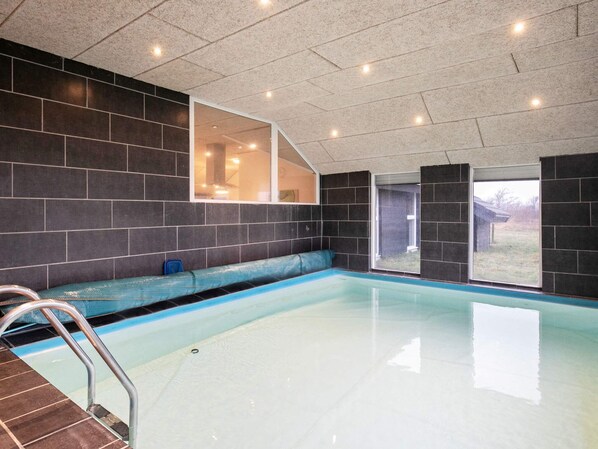 A modern indoor swimming pool with a clear view of the surrounding area, a built-in bench, and a ladder leading into the pool.