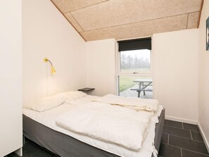 A bedroom with a bed, a bedside table, a lamp, and a window with a view of an outdoor picnic table. - 4 Star Holiday Home in Brovst (Brovst)