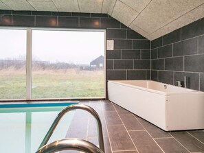 A modern bathroom with a large bathtub, a glass-enclosed shower area, and a view of a grassy field through a large window. - 4 Star Holiday Home in Brovst (Brovst)