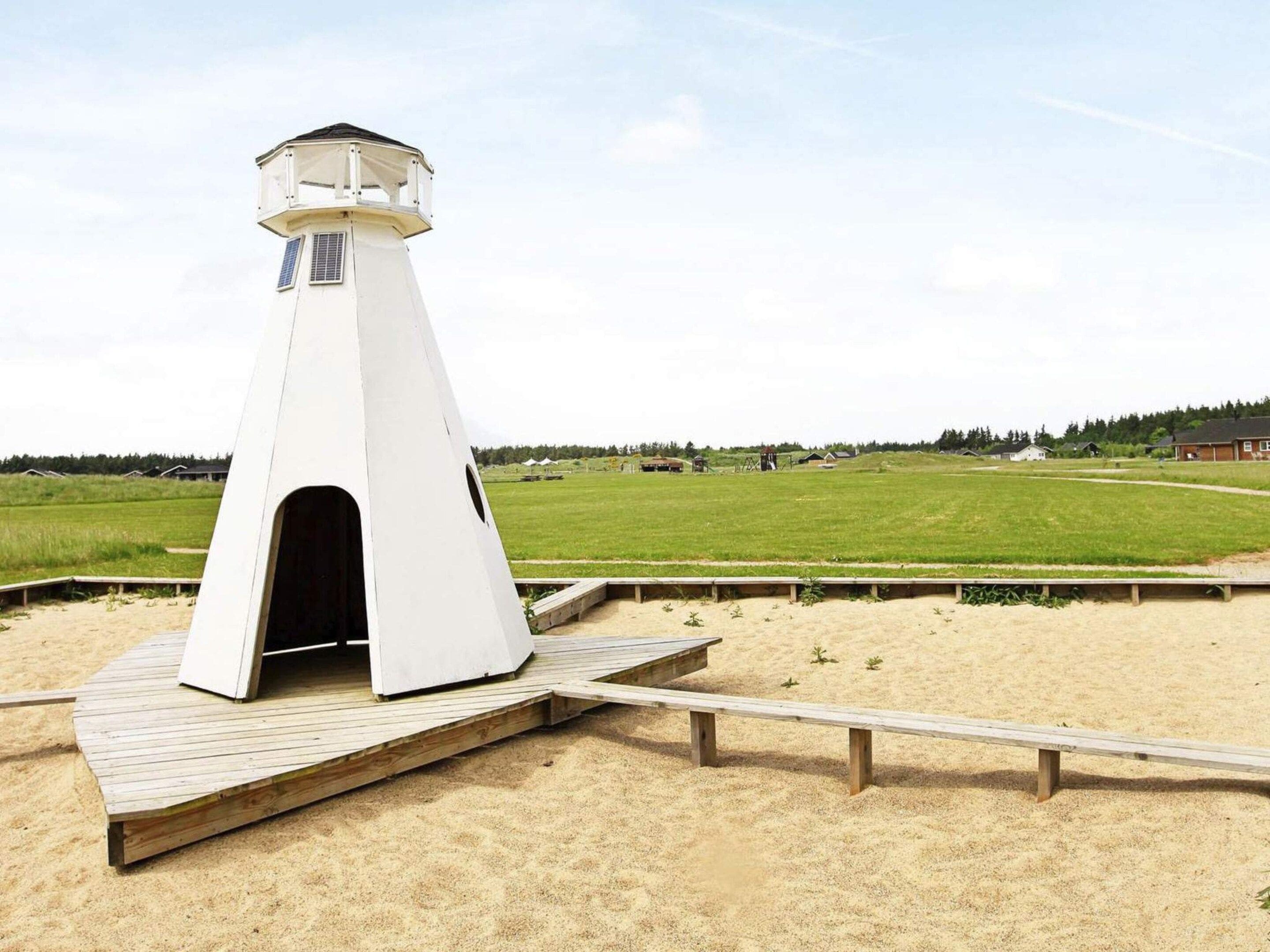 A white lighthouse on a wooden platform with a sandy beach in the background.