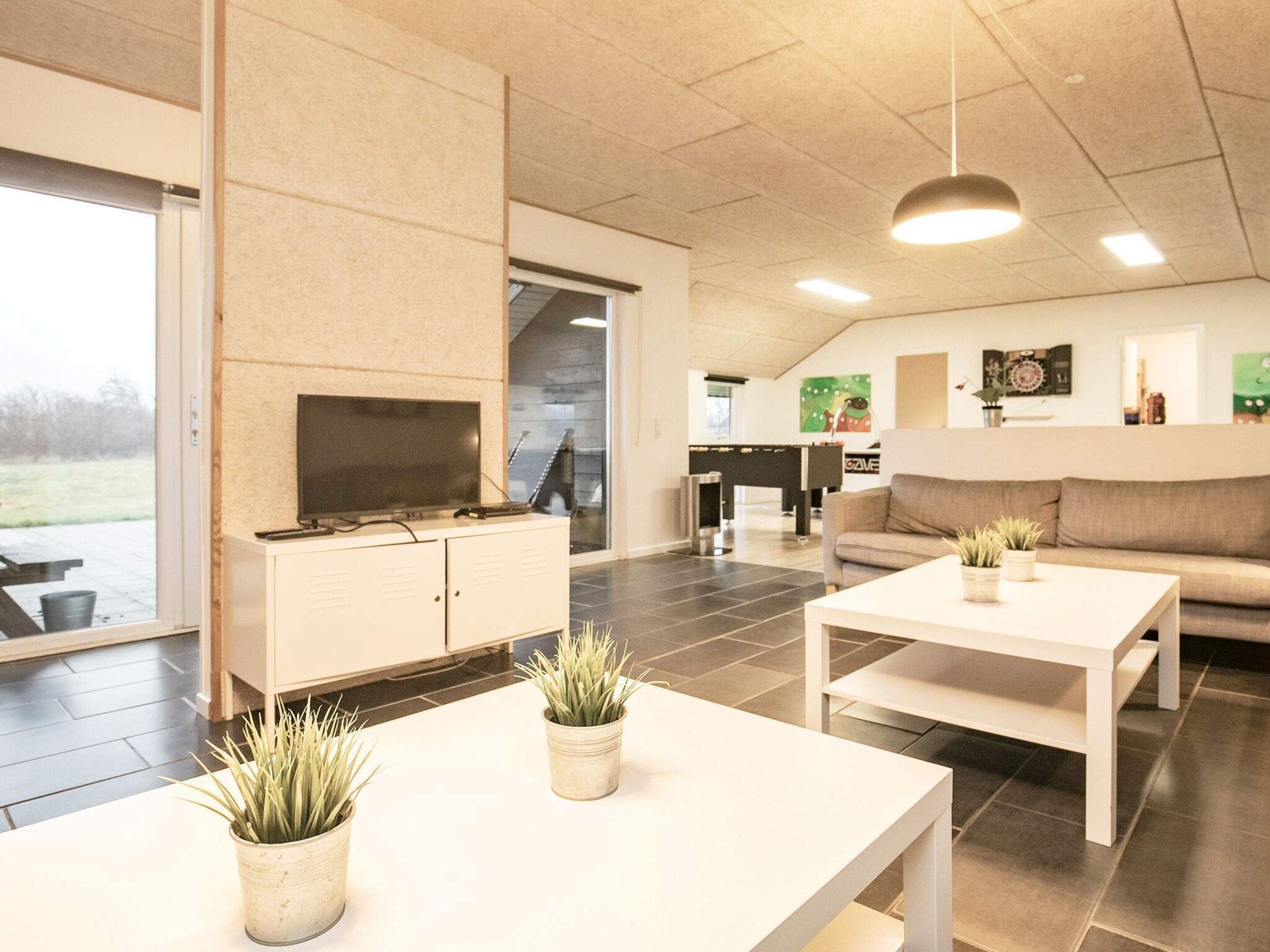 Uma sala moderna com televisão de tela plana, duas mesas de centro brancas, um sofá e um espaço de jantar com mesa e cadeiras.