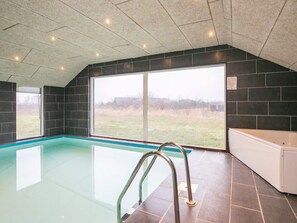 A swimming pool with a glass barrier, a white bathtub, and a view of a grassy field through large windows. - 4 Star Holiday Home in Brovst (Brovst)