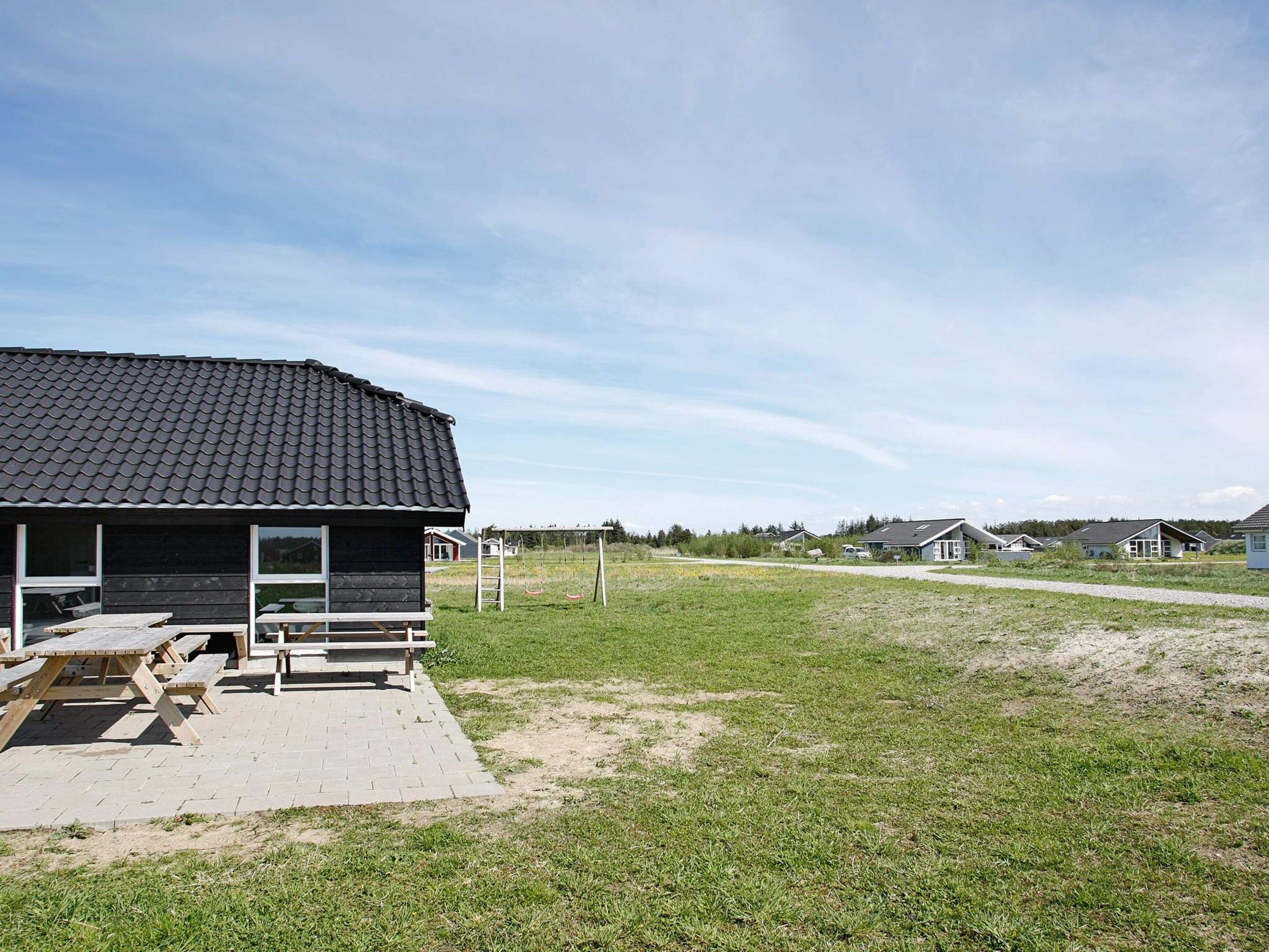 A residential area with a house featuring a dark roof and a porch with picnic tables.