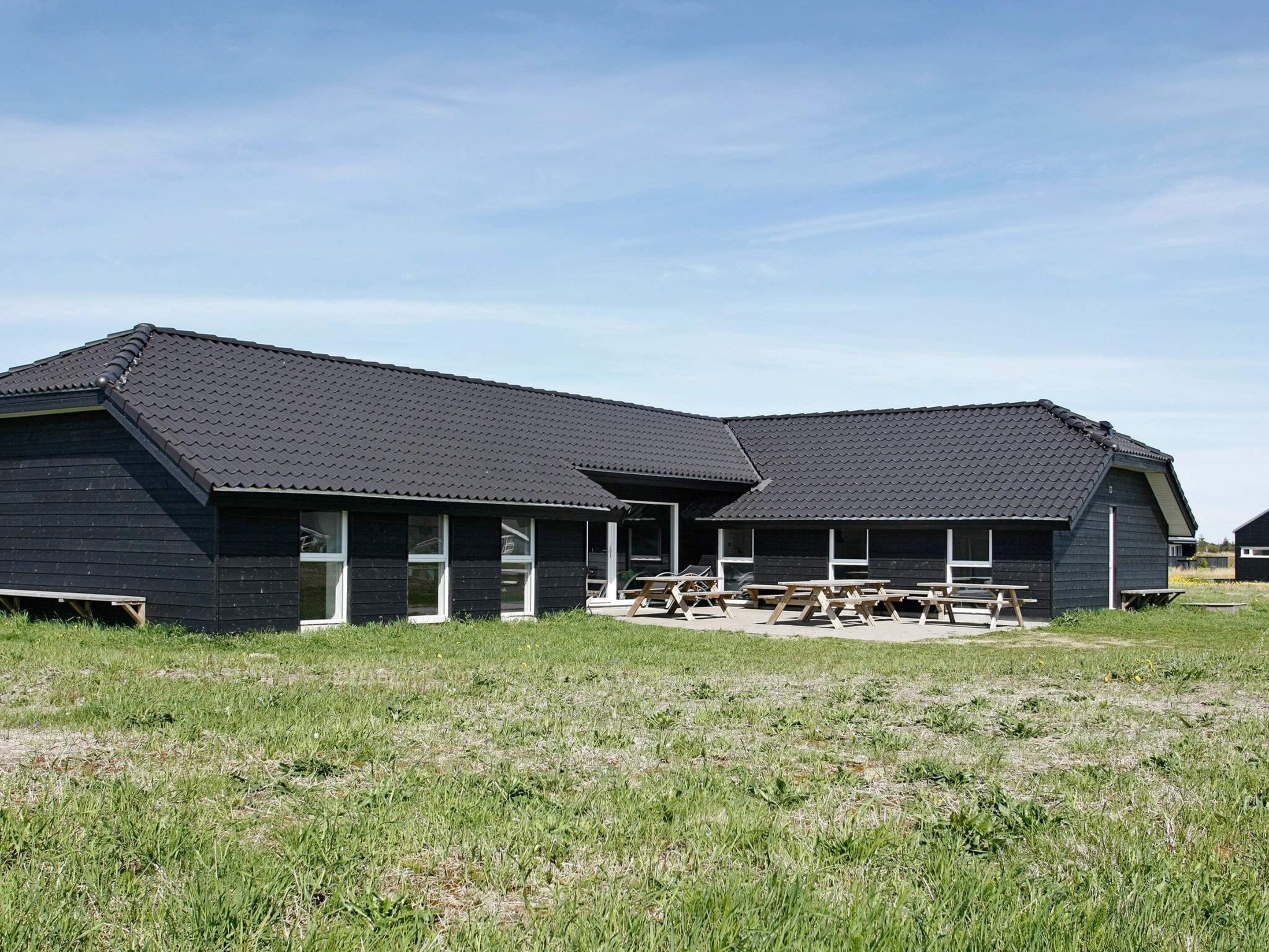 A two-story building with a dark roof and exterior walls, featuring a covered outdoor seating area with benches.