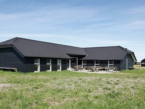 A two-story building with a dark roof and exterior walls, featuring a covered outdoor seating area with benches.