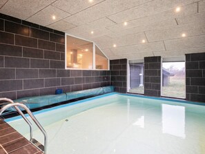 A modern indoor swimming pool with a clear water surface, a built-in bench, and a metal ladder.