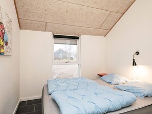 A bedroom with a bed, a window, a wall-mounted lamp, and a painting.