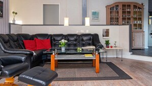 A modern living room with a black leather sofa, a glass coffee table, and a wooden cabinet in the background. - Luxury Spa Retreat - By Traum Ferienwohnungen (Glesborg)