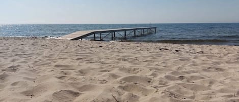 Una playa arenosa con un muelle de madera que se adentra en el agua.