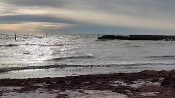 Ein Strand mit rauen Wellen und einem dazugehörigen, felsigen Wellenbrecher im Hintergrund.