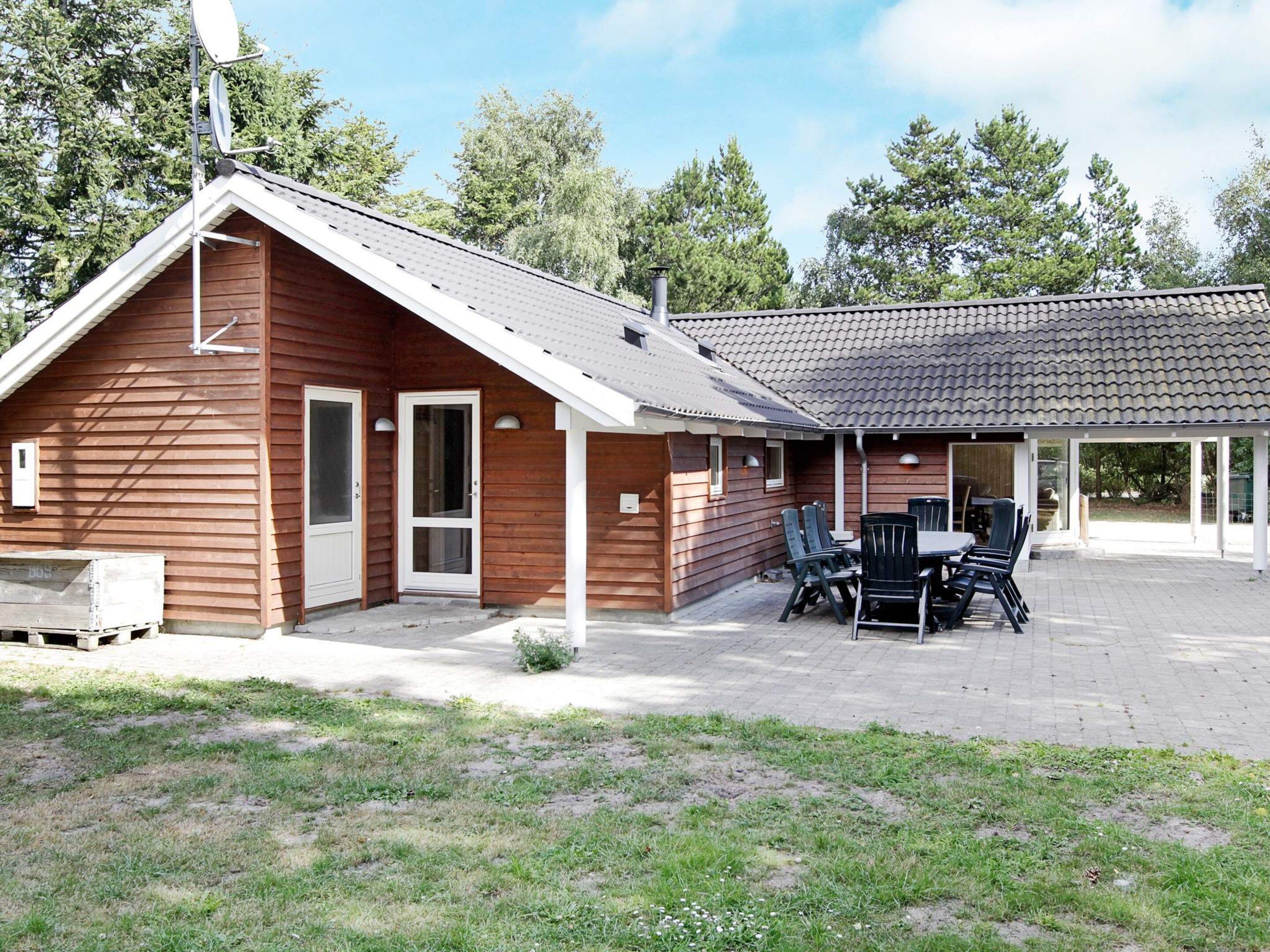 Eine Holzhütte mit überdachter Terrasse, einem Esstisch mit Stühlen und einer Satellitenschüssel.