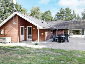 A wooden cabin with a covered patio area, a dining table with chairs, and a satellite dish.