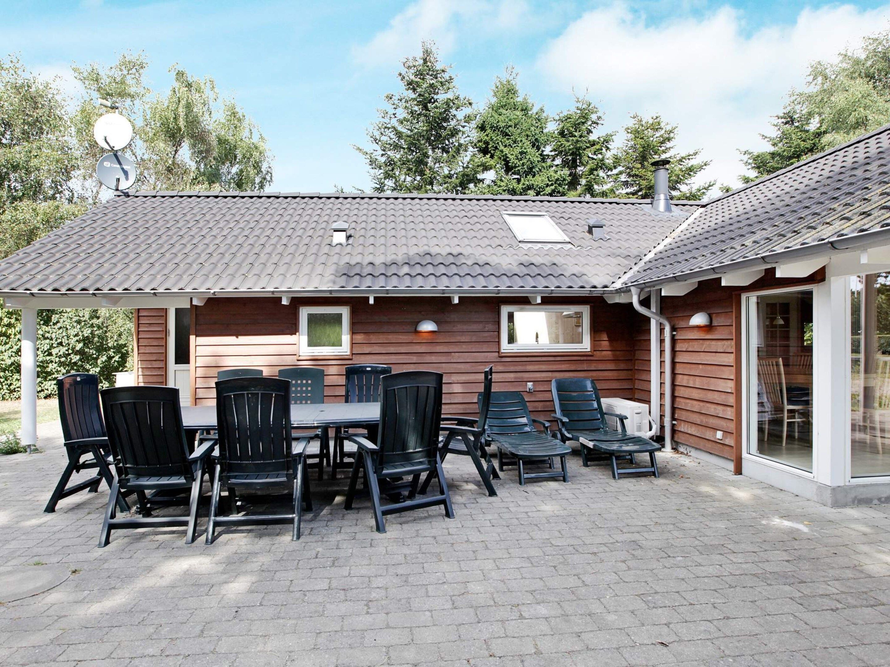 A wooden cabin with a tiled roof, a patio with a table and chairs, and a glass door leading to an interior space.