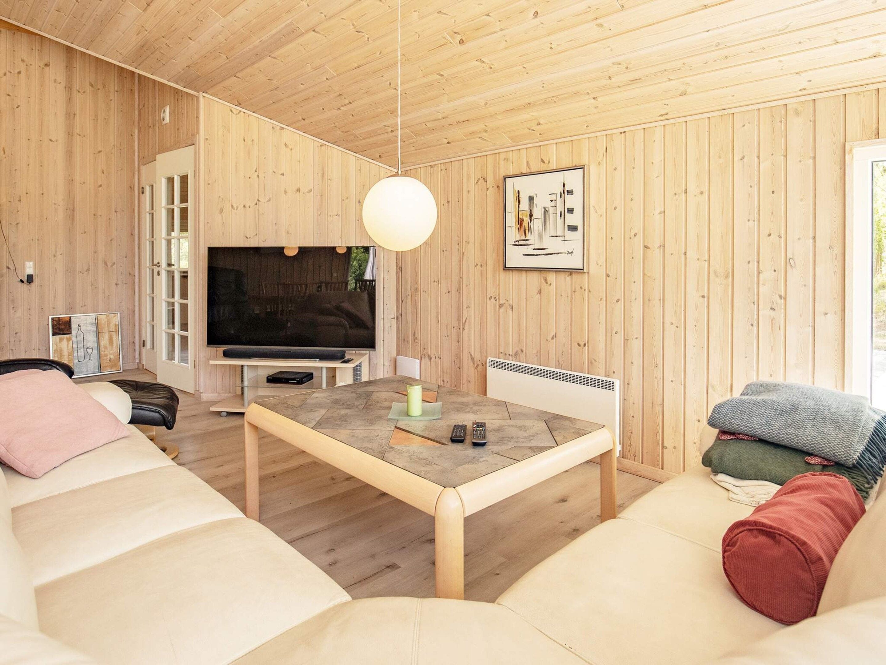 Een moderne woonkamer met houten inrichting, een flatscreen televisie, een eettafel en een bank.