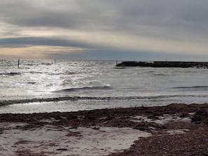 A coastal scene with rough sea waves, a rocky shoreline, and a breakwater structure.