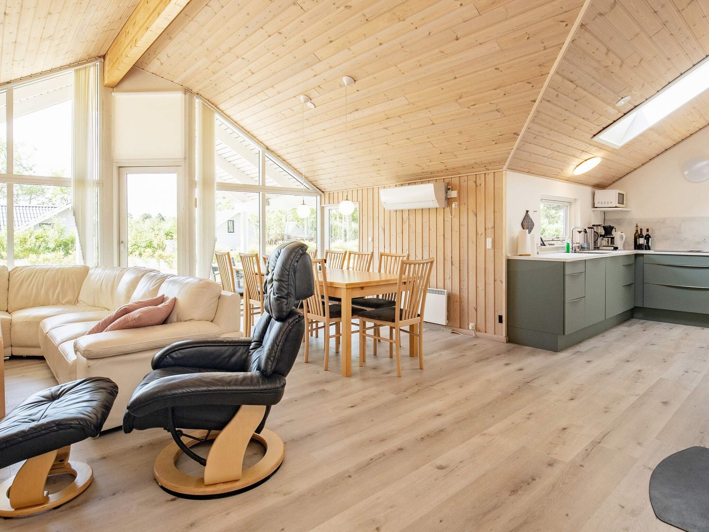 A modern interior with a wooden ceiling, a dining area with a table and chairs, a sofa, a massage chair, and a kitchen area.