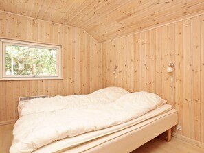 A single bed in a room with wooden walls and a window.