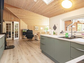 Een moderne keuken met houten vloeren, een eethoek met een zwarte stoel, en een groot raam dat voor natuurlijk licht zorgt.