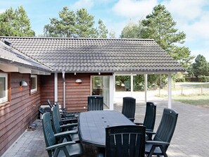 An outdoor patio with a table and chairs, a covered area, and a view of trees and a road.