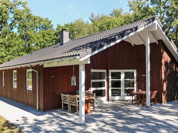 A wooden cabin with a covered patio, large windows, and a chimney.