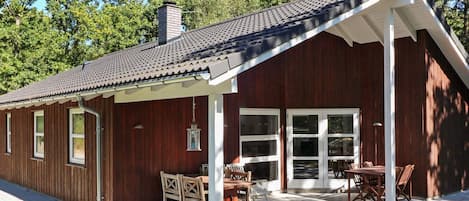 A wooden cabin with a covered patio, large windows, and a chimney.