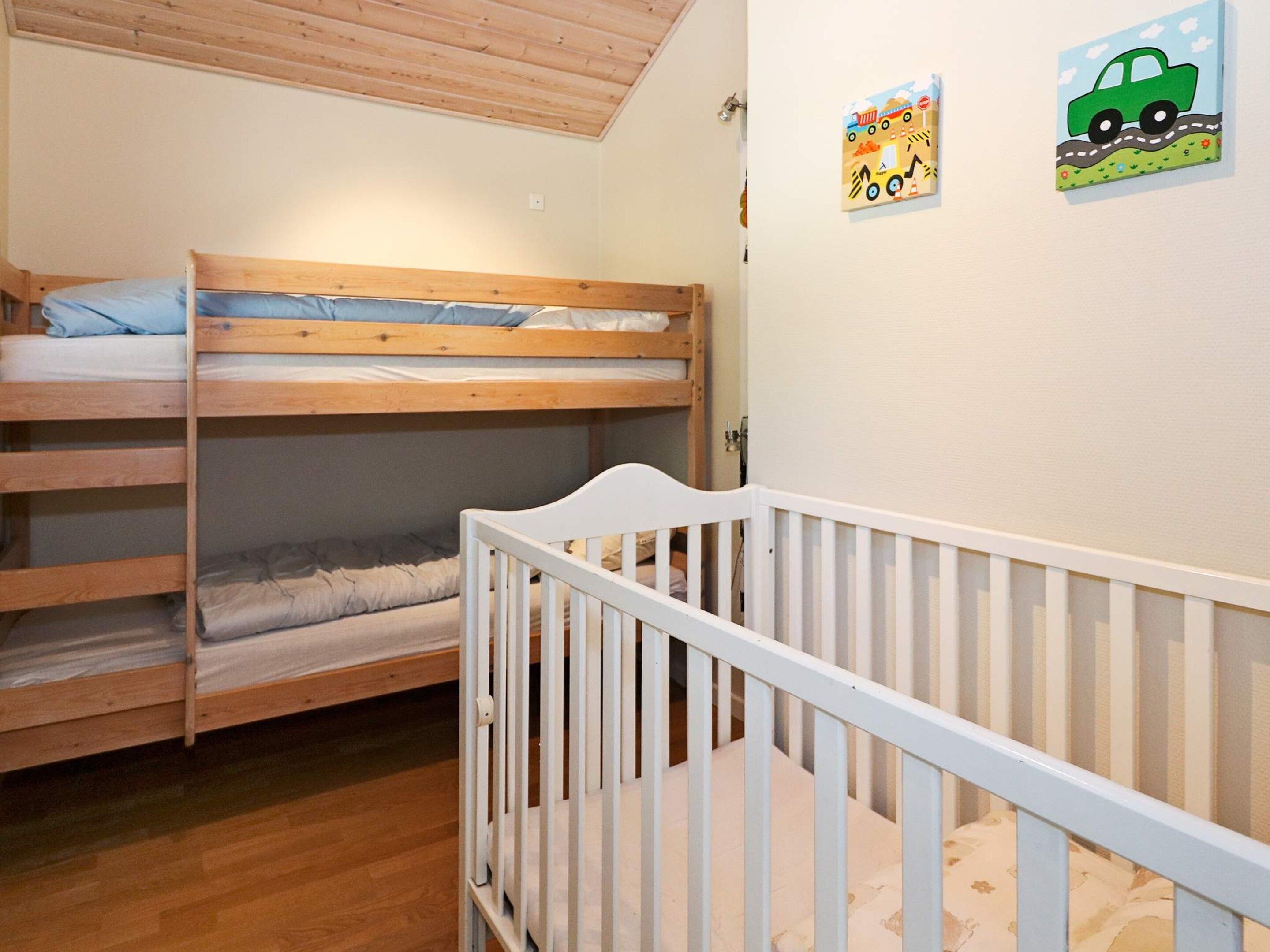 A bunk bed room with a white crib in the foreground and two children's artwork on the wall.