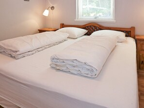 A double bed with a wooden headboard, two bedside tables, a wall-mounted lamp, and a window with a view of trees.