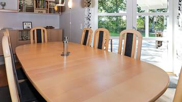 A conference room with a large oval table, six chairs, pendant lighting, a bookshelf, and a view of the outdoors through large windows.