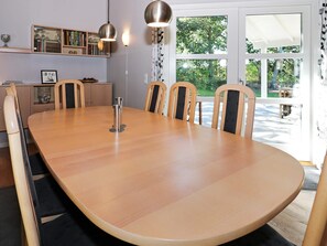 A conference room with a large oval table, six chairs, pendant lighting, a bookshelf, and a view of the outdoors through large windows.