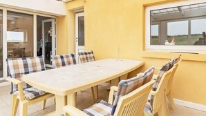 Eine sonnendurchflutete Terrasse mit Tisch und Stühlen, einer Schiebetür und Blick auf die Landschaft.