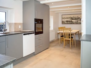A modern kitchen with a built-in oven, a dining area with a table and chairs, and a large window providing natural light. - 11 Person Holiday Home in Thisted (Thisted)