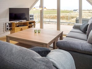 A modern living room with a large TV, wooden coffee table, grey sofa, and a view of the outdoors.