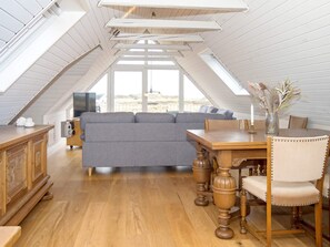 A loft-style room with a wooden floor, a grey sofa, a wooden dining table with chairs, and a TV on a wooden cabinet. - 11 Person Holiday Home in Thisted (Thisted)