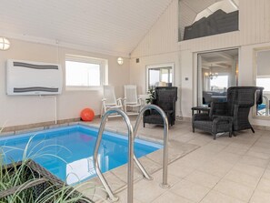 An indoor swimming pool with a metal ladder, white chairs, and wicker furniture. - 11 Person Holiday Home in Thisted (Thisted)