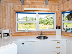 A kitchen with wooden walls, a white countertop, a Bosch dishwasher, a sink, and two windows with a view of greenery and buildings.