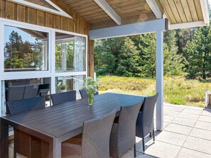 An outdoor patio with a wooden table and chairs, surrounded by glass walls. - 4 Star Holiday Home in Fjerritslev (Fjerritslev)