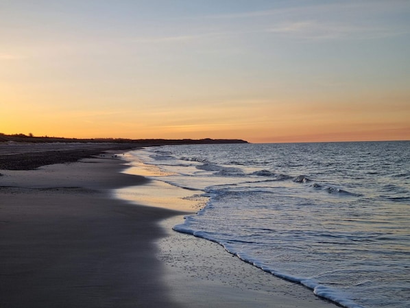 A beach with a calm sea, a sandy shore, and a distant landmass.