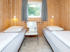 Una habitación con dos camas, una silla, una ventana con cortinas e iluminación en la pared.