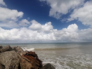 Una playa con grandes rocas al frente y un cielo despejado con nubes.