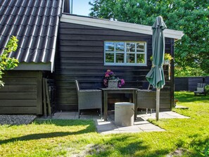 A house with a dark exterior, a window, a patio with a table and chairs, and a green umbrella. - Attractive Holiday Home in Hemmet near Sea (Hemmet)